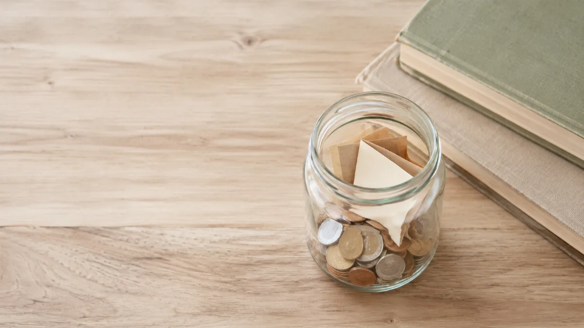 Glass jar holding folded notes and coins on a wooden surface