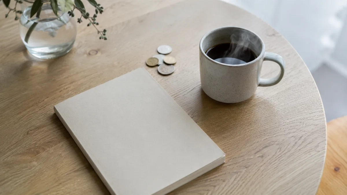 Kitchen table with a plain notebook, a few coins and a cup of coffee