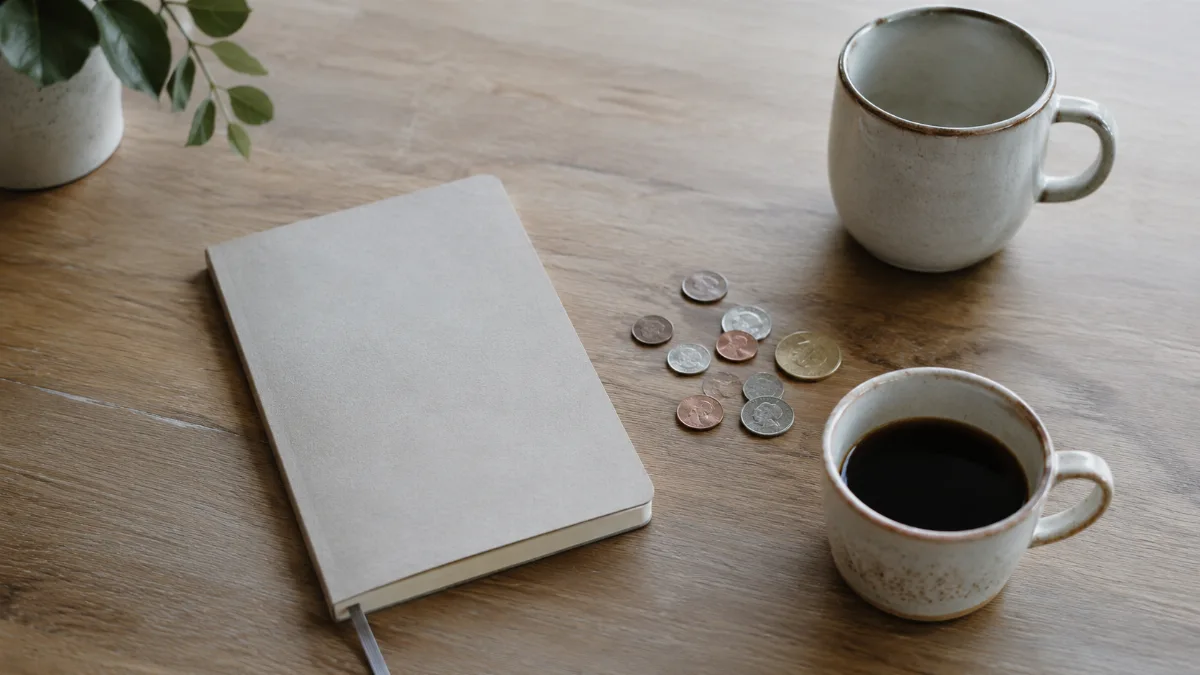 Kitchen table with a plain notebook, coins and a coffee cup