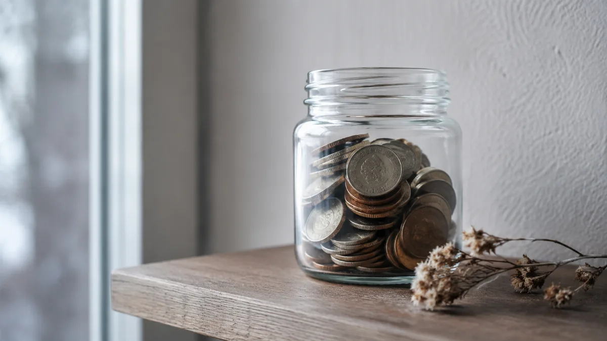 Glass jar of saved coins on a wooden shelf
