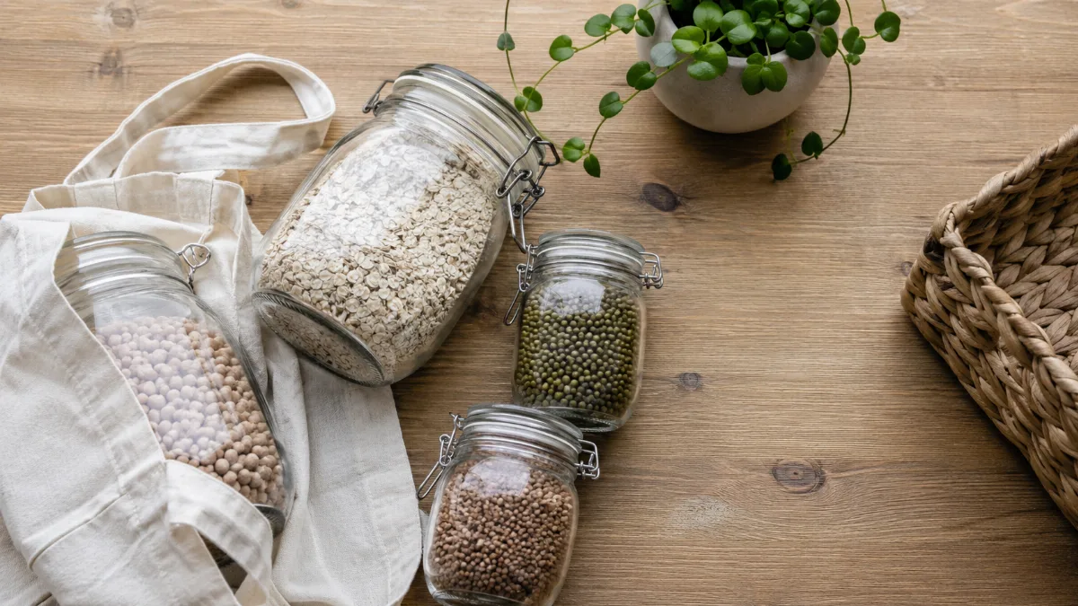 Reusable glass jars, a cloth bag and a small potted plant on a wooden surface