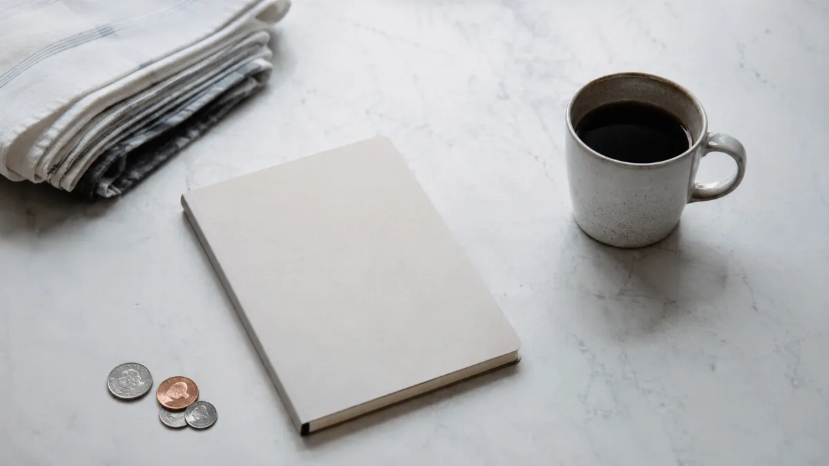 Kitchen table with a plain notebook, a few coins and a cup of coffee