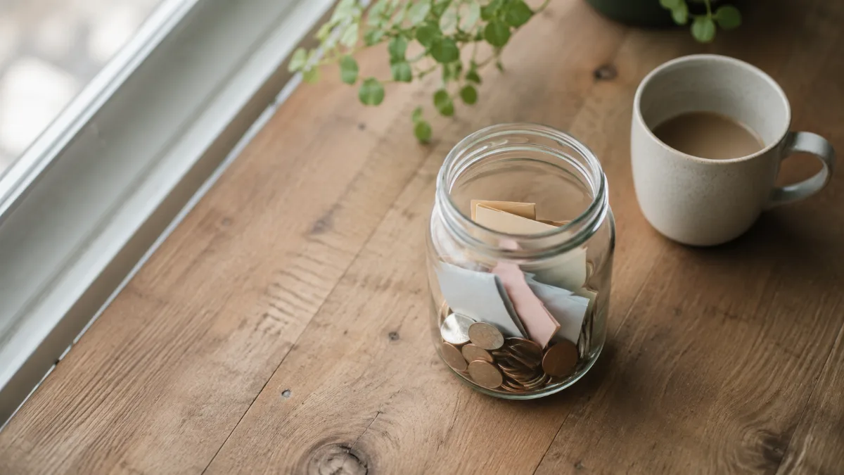 Glass jar holding folded notes and coins on a wooden surface