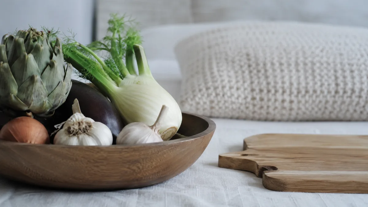 Wooden bowl of vegetables beside a chopping board